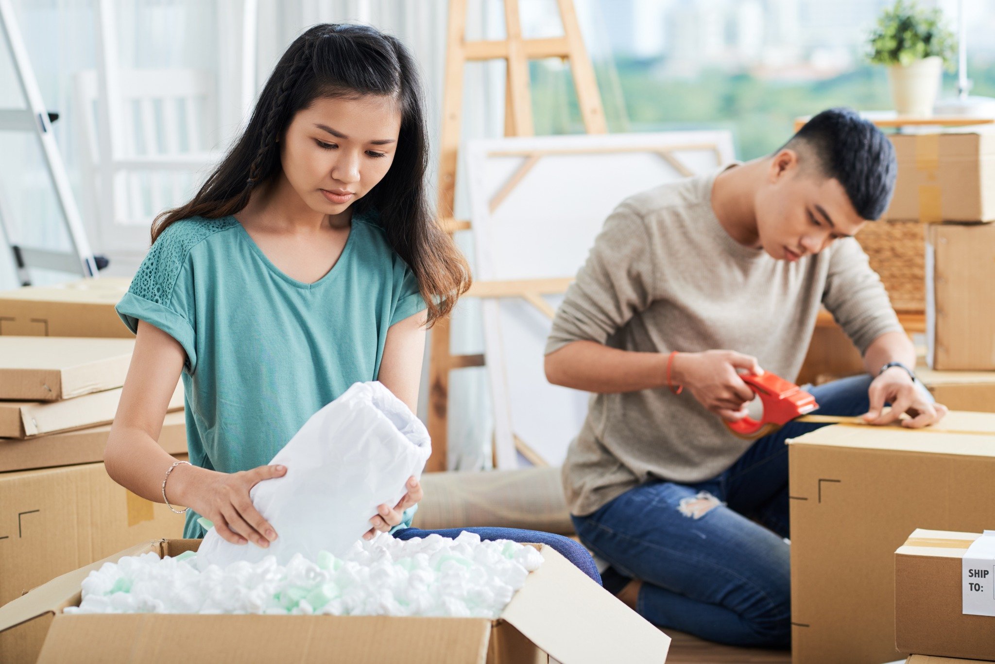 A couple carefully packs household items into moving boxes, wrapping fragile belongings for safe transport during a move to their new home.