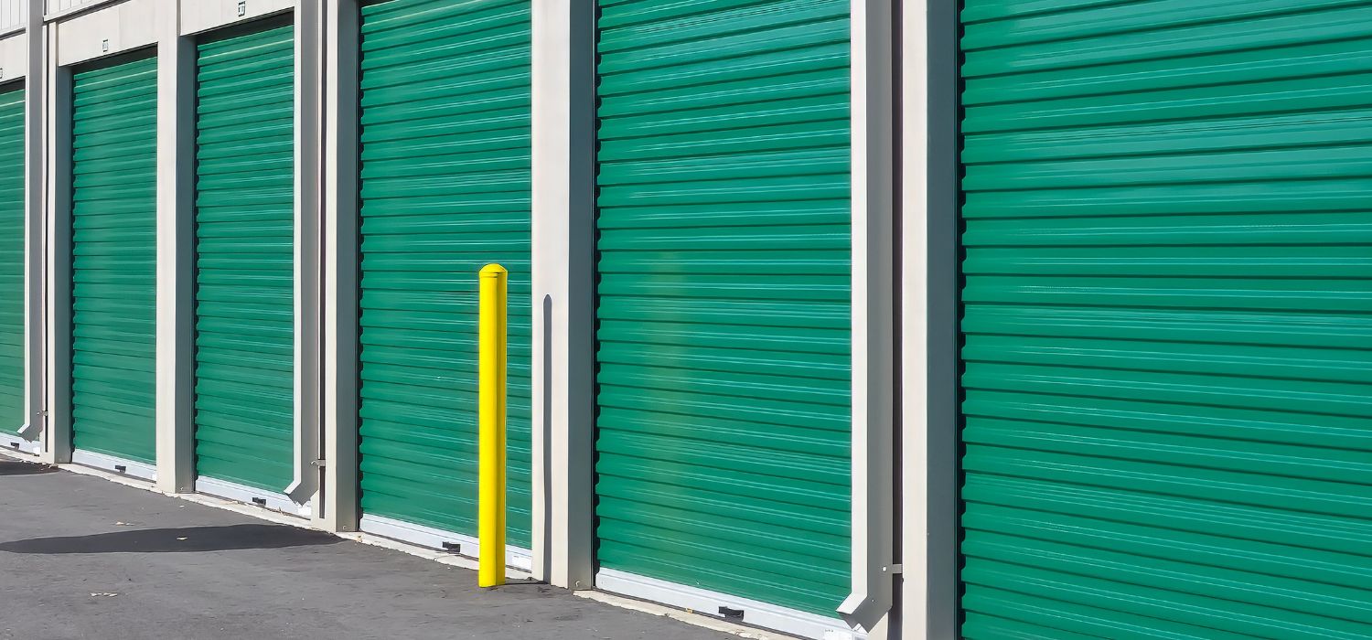 A row of green roll-up doors at a self-storage facility, showing multiple secure storage units used for storing belongings during a move.